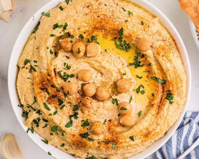 overhead photo of a large white serving bowl filled with homemade hummus topped with chickpeas and olive oil.