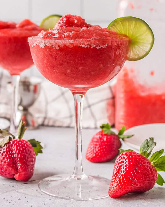 two glasses of frozen margaritas on a counter with fresh strawberries.