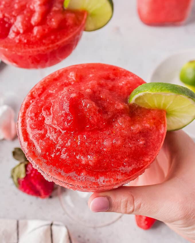 holding a glass of frozen strawberry margarita garnished with a lime slice