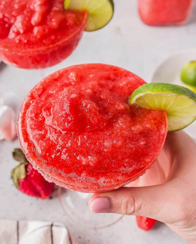 holding a glass of frozen strawberry margarita garnished with a lime slice