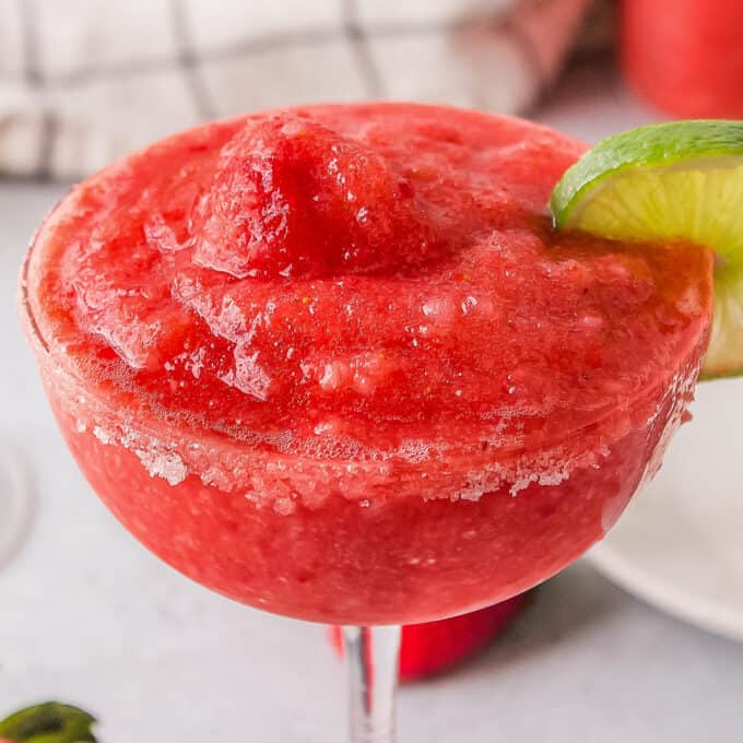 close up photo of a frozen strawberry margarita in a glass with a sugar rim and lime slice.