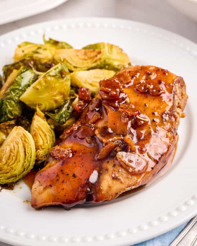 white plate with a glazed chicken breast alongside some brussels sprouts.