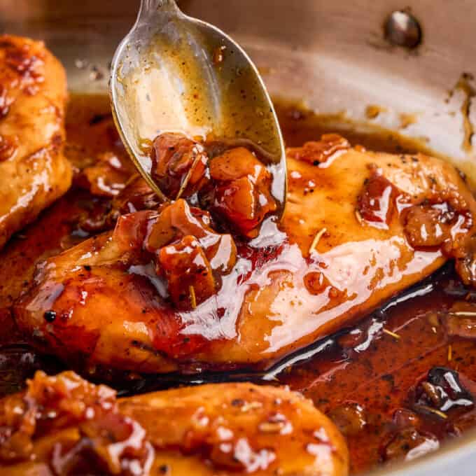 spooning bacon glaze over a cooked chicken breast in a stainless steel skillet.