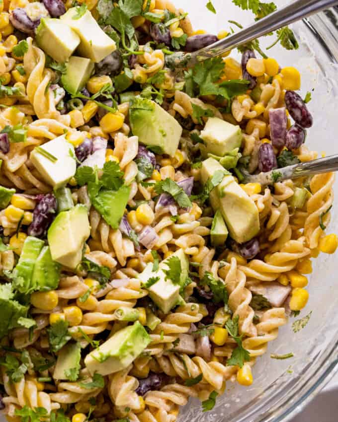 overhead photo of street corn pasta salad in a glass bowl with serving spoons.