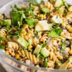 glass bowl filled with street corn pasta salad garnished with avocado and cilantro