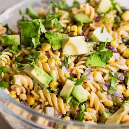 glass bowl filled with street corn pasta salad garnished with avocado and cilantro