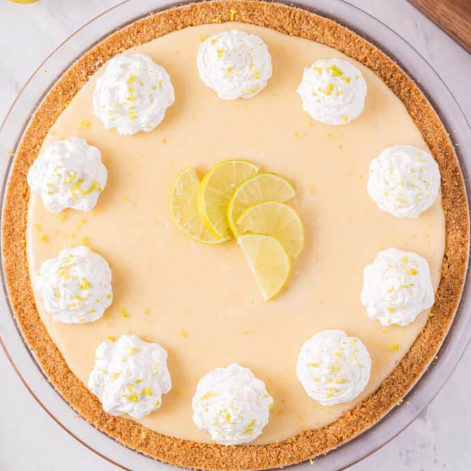 overhead photo of a key lime pie with whipped cream dollops and lime slices.