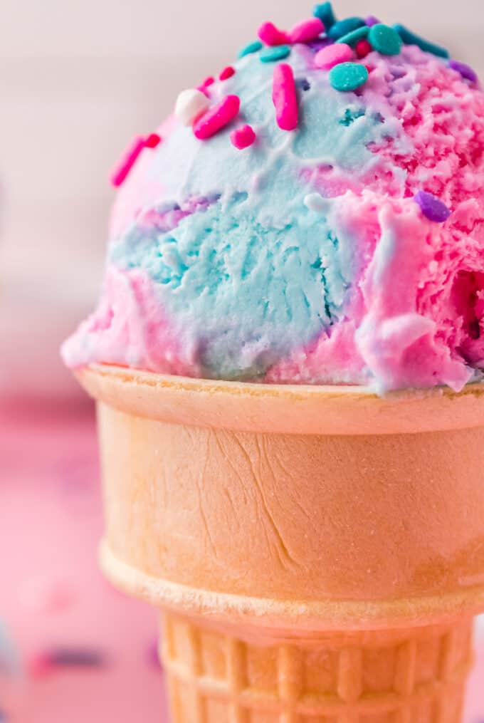 ice cream cone with a scoop of cotton candy ice cream with sprinkles on top.