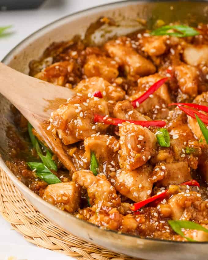 Wooden spoon stirring a skillet full of black pepper chicken.