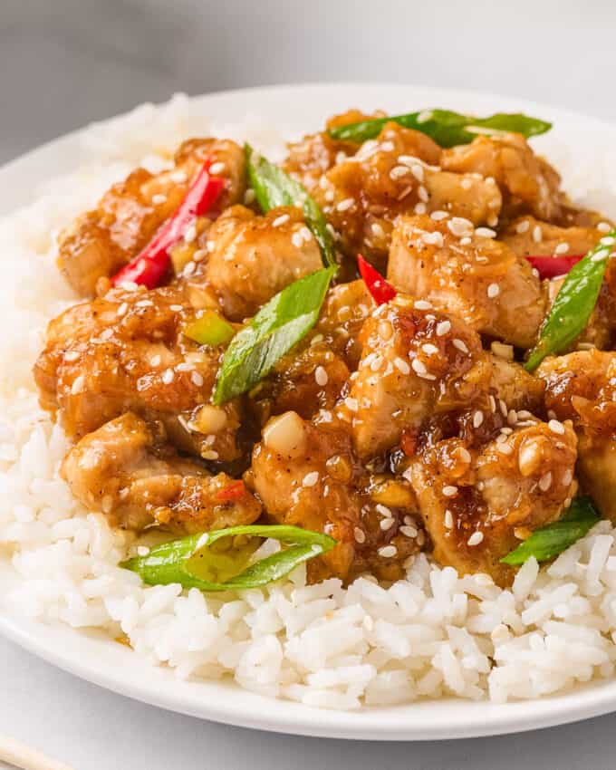 White plate topped with white rice and black pepper chicken garnished with sesame seeds and green onion.