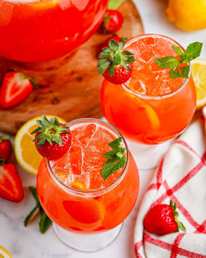 Glass pitcher of homemade lemonade with fresh strawberries, alongside two glasses.