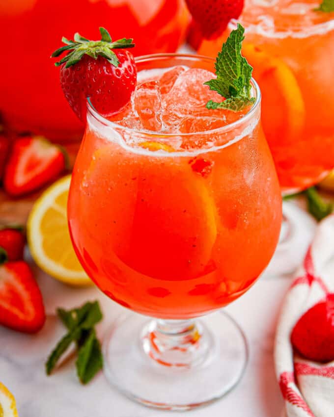 Close photo of a glass of cold strawberry lemonade with a sprig of mint and a strawberry.