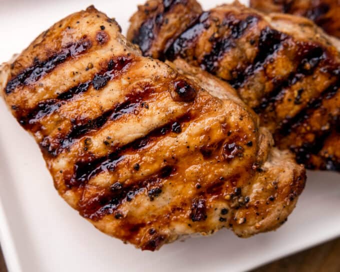 several grilled pork chops on a white platter with dark grill marks.