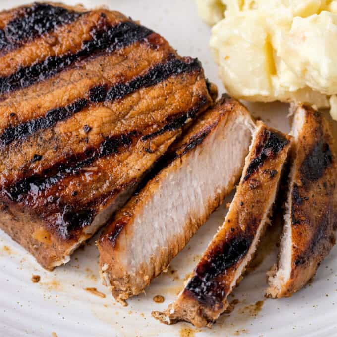 grilled pork chop that's been partially sliced on a plate with potato salad.