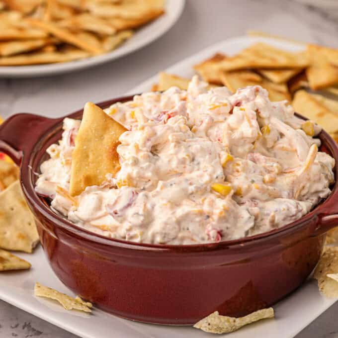 serving bowl of boat dip with a pita chip dipped in it.