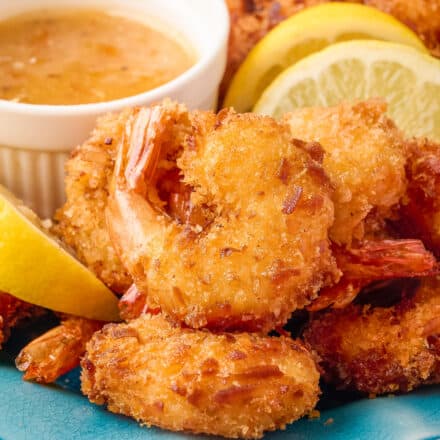 coconut shrimp on blue plate with lemon wedges and a dipping sauce in white ramekin.
