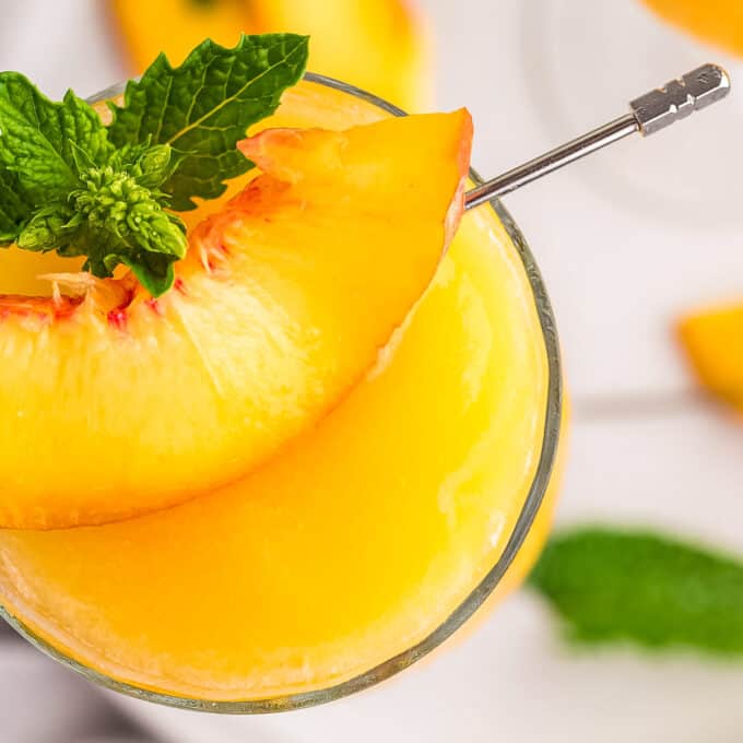 Overhead view of frozen peach bellini that's garnished with a fresh peach slice and sprig of mint.