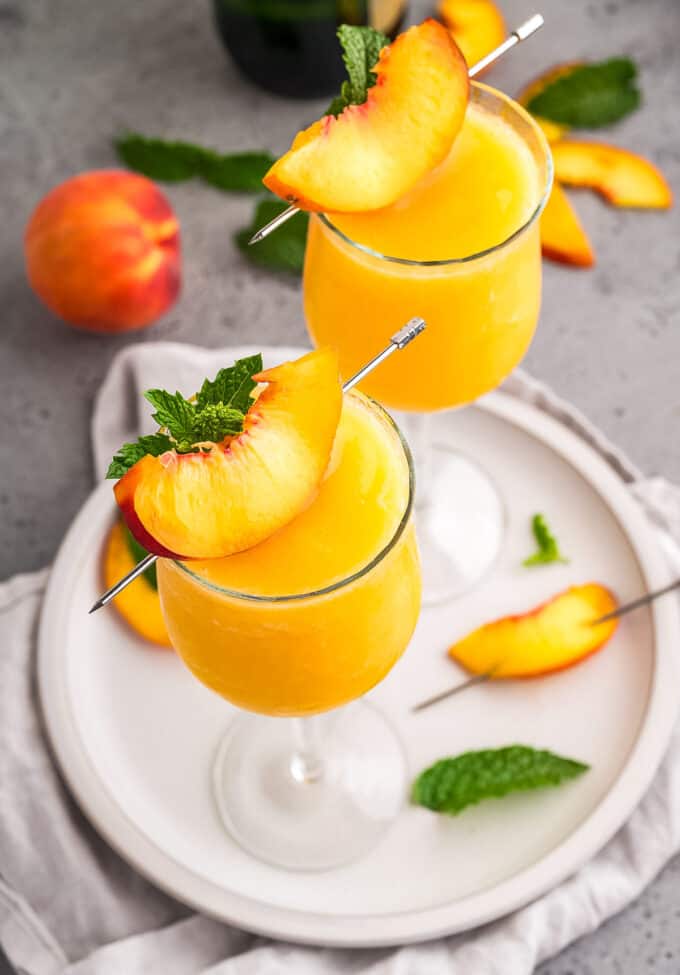 Two wine glasses full of peach bellinis on a white serving plate.