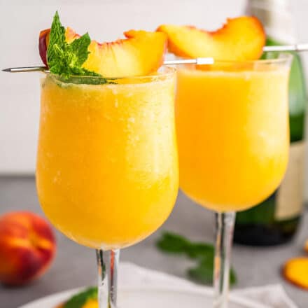 two frosty wine glasses filled with frozen peach bellinis topped with a peach slice.