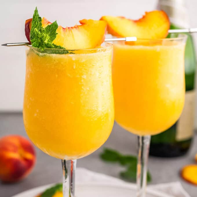 two frosty wine glasses filled with frozen peach bellinis topped with a peach slice.