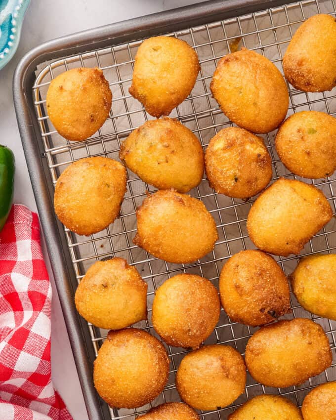 overhead photo of fried hush puppies on a wire rack topped baking sheet.