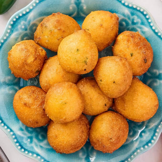 overhead photo of a pile of fried hush puppies on a blue scalloped plate.