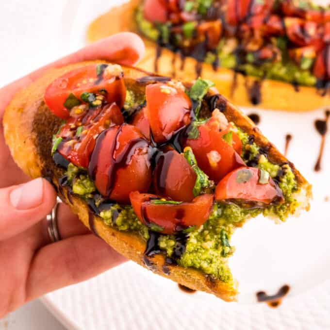 Hand holding a slice of bruschetta with pesto, with a bite taken out of it.