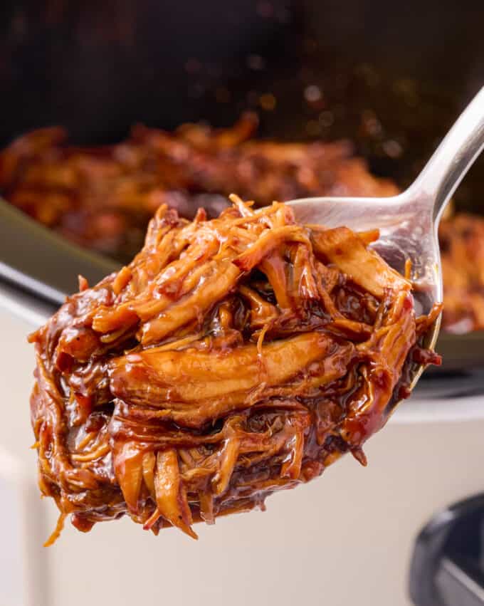 serving spoon of saucy teriyaki chicken taken out of a slow cooker.