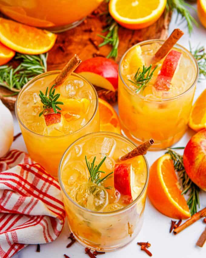 several glasses of fall punch on a white table with garnishes.