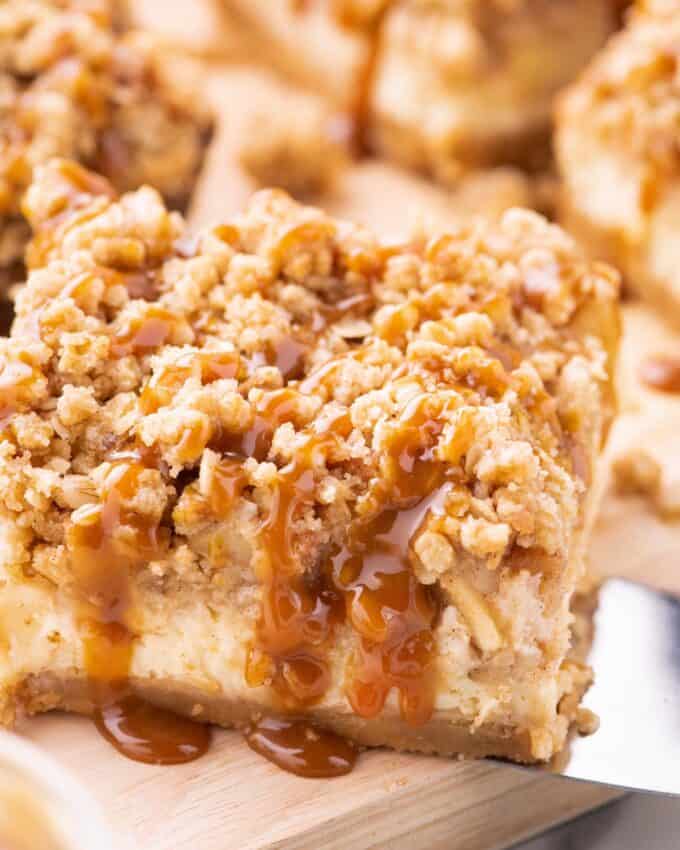 spatula serving a apple cheesecake bar drizzled with caramel sauce.