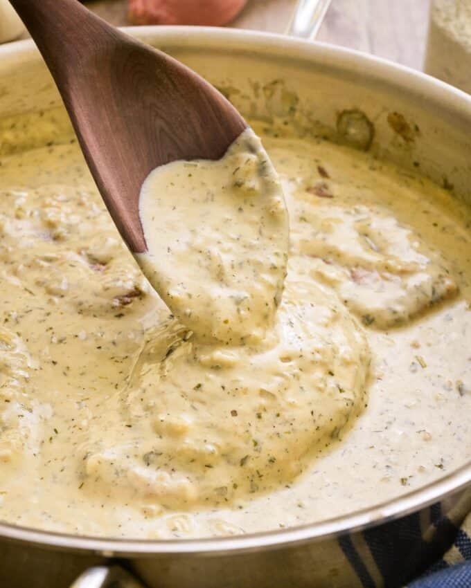 spooning creamy ranch sauce over pork chops in a skillet.
