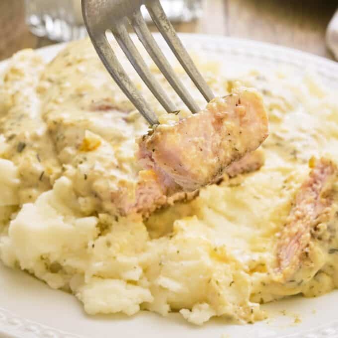 forkful of ranch smothered pork chops over mashed potatoes.