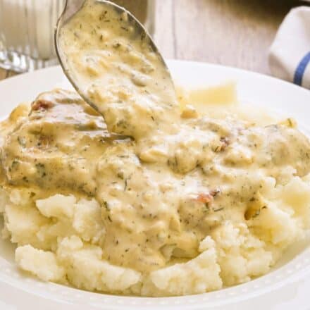 spooning ranch sauce over a smothered pork chop on top of a bed of mashed potatoes.