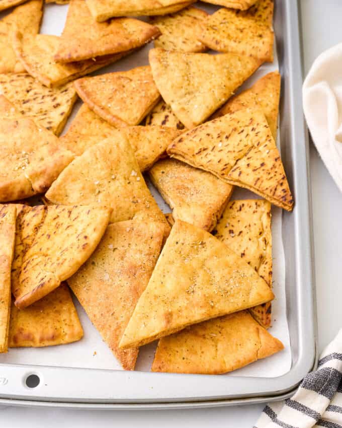 close up photo of homemade pita chips on baking sheet with a kitchen towel next to it.