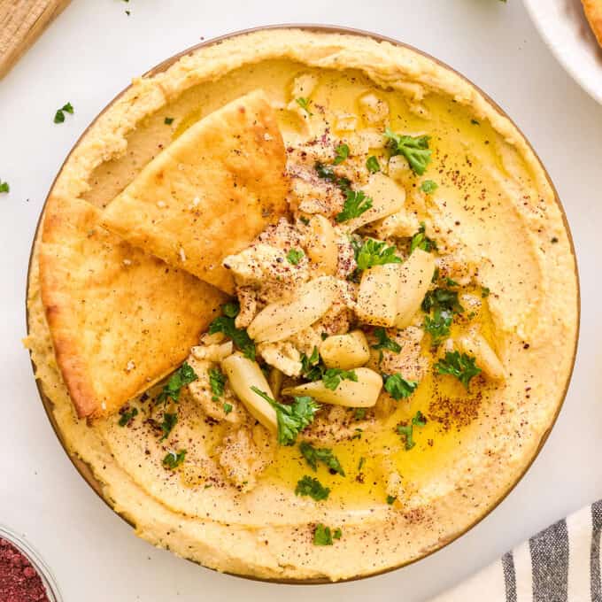 overhead photo of roasted garlic hummus in shallow bowl, with 2 pita chips dipped into the bowl.