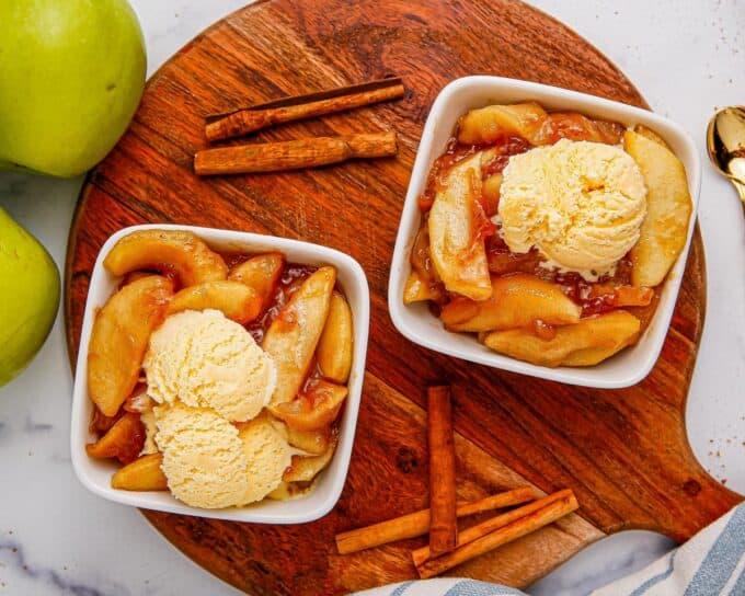 round serving board topped with two white bowls of fried apples with ice cream.