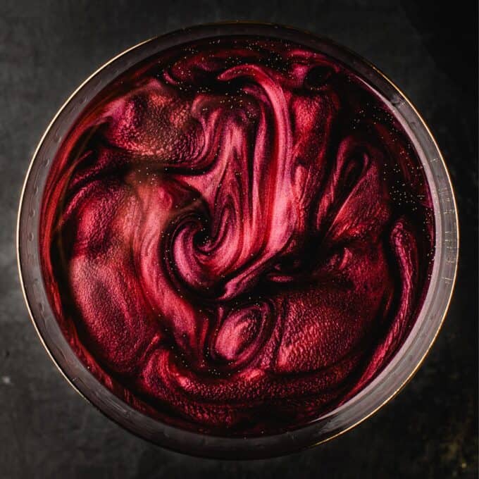 overhead photo of a black vodka martini with red and gold luster dust swirled into it.