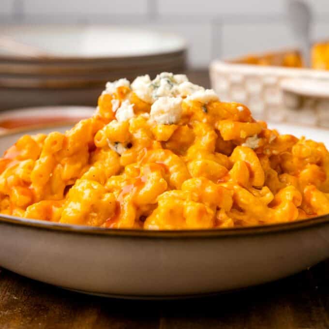 shallow bowl filled with buffalo chicken mac and cheese topped with hot sauce and blue cheese.