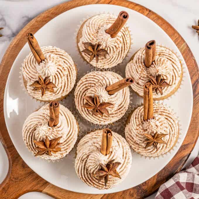 round wooden cutting board topped with a white plateful of chai latte cupcakes.
