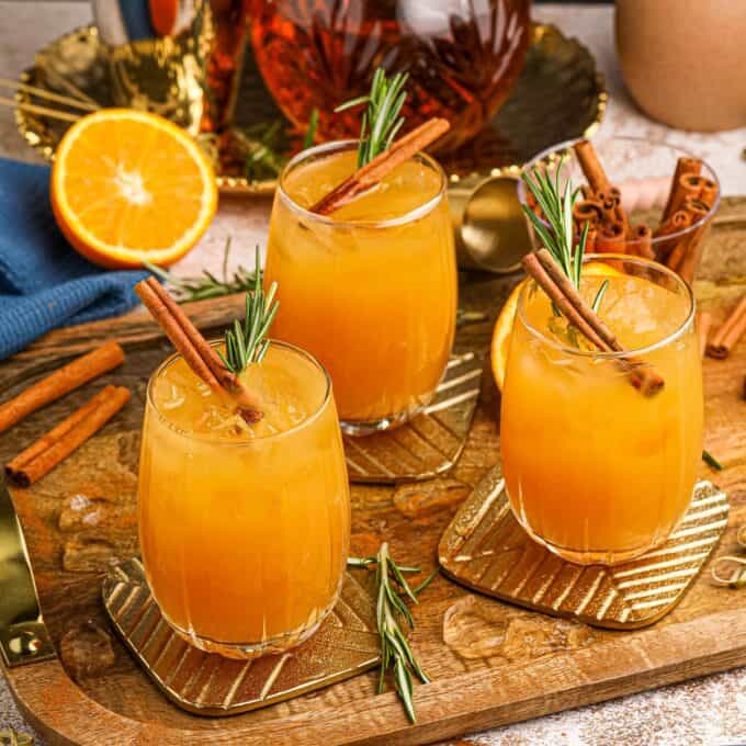 a serving tray with three whiskey sour cocktails on it, surrounded by garnishes, linens, and decanters.