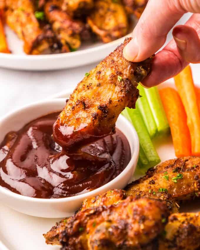 dipping a chicken wing into a small bowl of barbecue sauce.