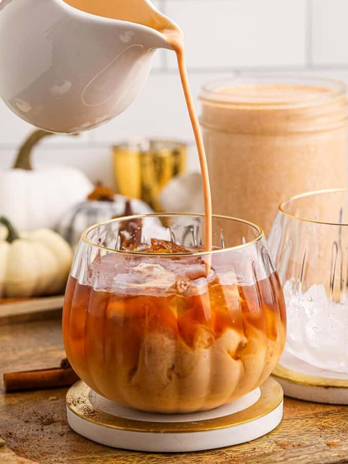 pouring pumpkin spice creamer into a glass of iced coffee.