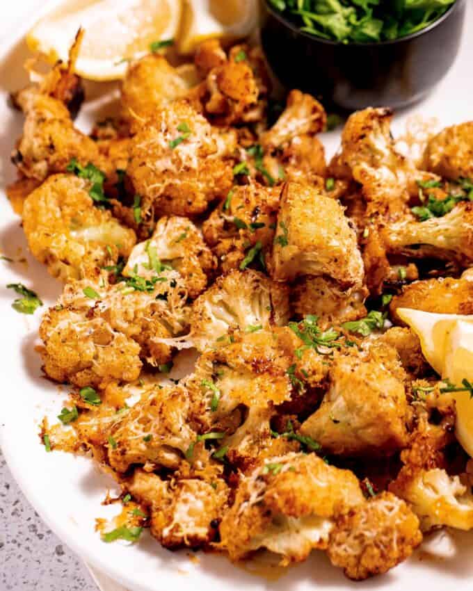 white platter of roasted cauliflower sprinkled with parsley and alongside some lemon wedges.