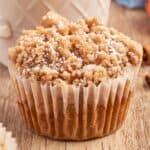 pumpkin muffin topped with streusel with a parchment paper wrapper and a cup of coffee.