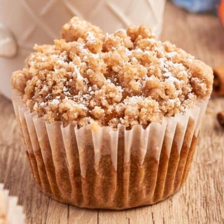 pumpkin muffin topped with streusel with a parchment paper wrapper and a cup of coffee.
