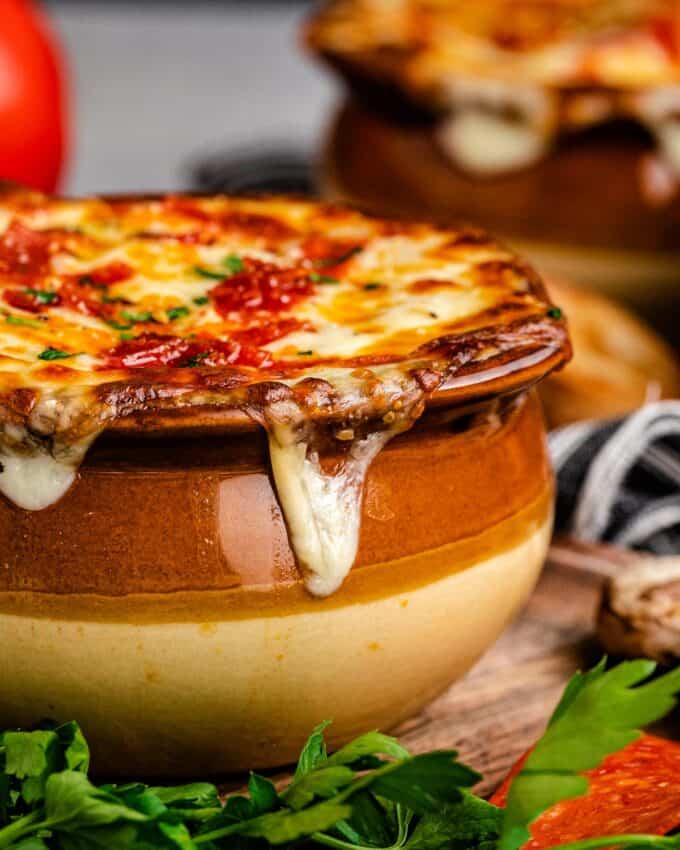 side view of a crock of pizza soup with gooey baked cheese on top.