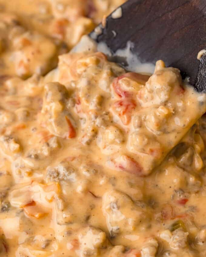 wooden spoon stirring a skillet full of cheesy sausage dip with rotel