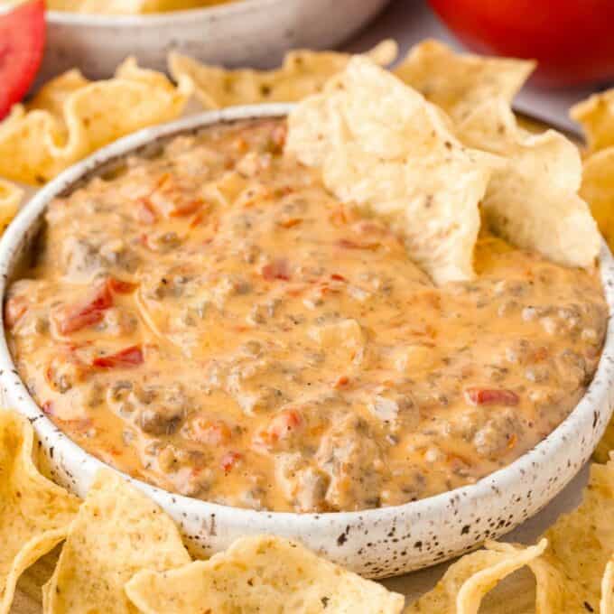 white bowl filled with velveeta sausage dip surrounded with tortilla chips