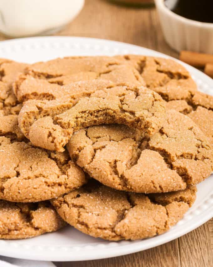 pile of molasses cookies on a white plate with a bite taken out of one.