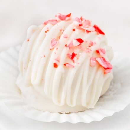candy cane cake ball on a liner, drizzled with white chocolate and sprinkled with crushed candy canes.